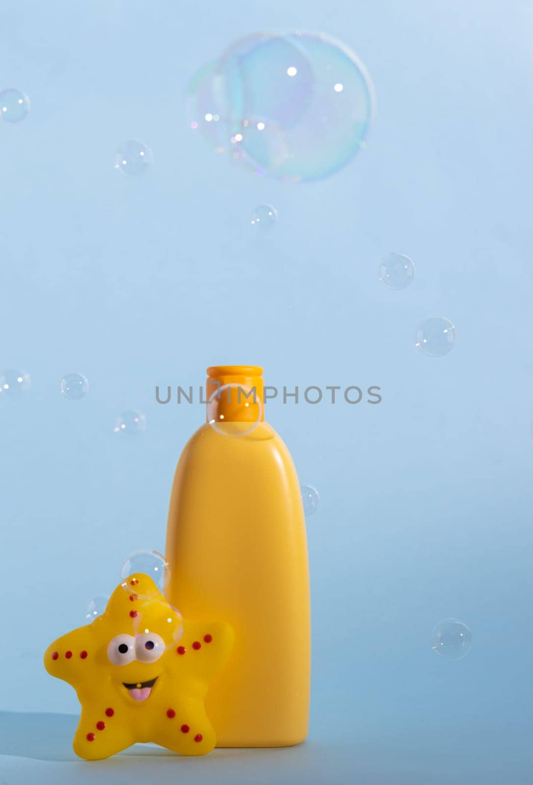 Empty yellow plastic bottle with soap or shampoo on a light blue background with flying soap bubbles.. by Ri6ka