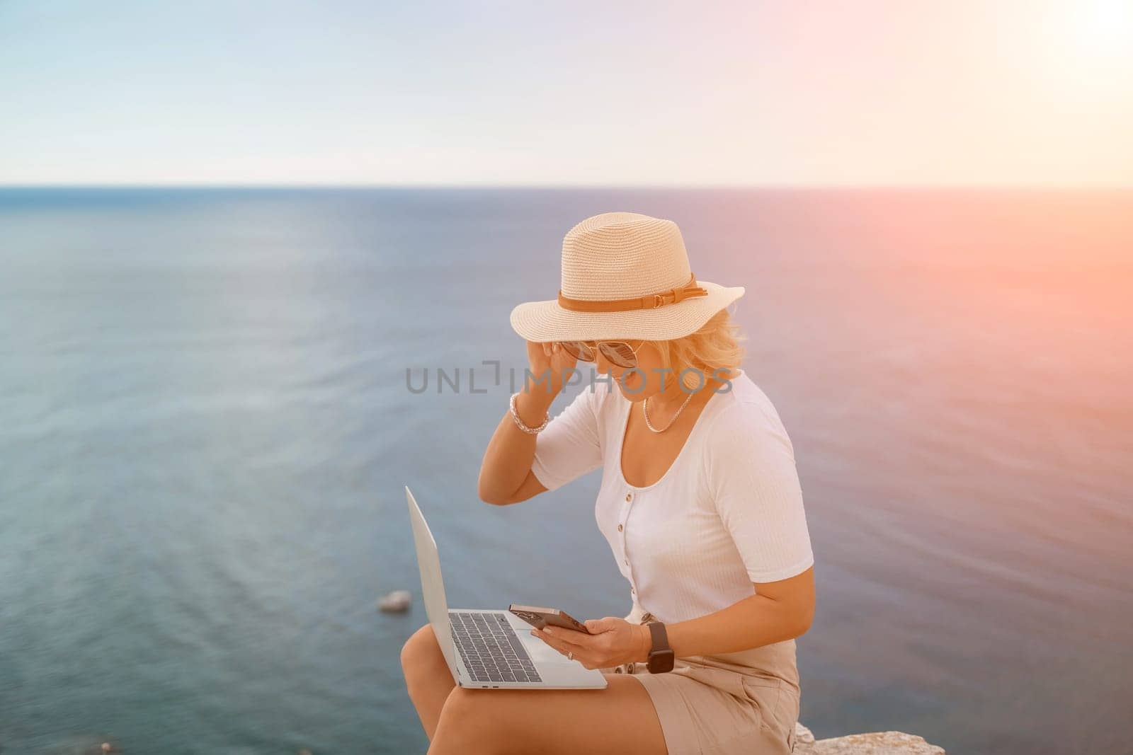 Freelance women sea working on the computer. Good looking middle aged woman typing on a laptop keyboard outdoors with a beautiful sea view. The concept of remote work. by Matiunina