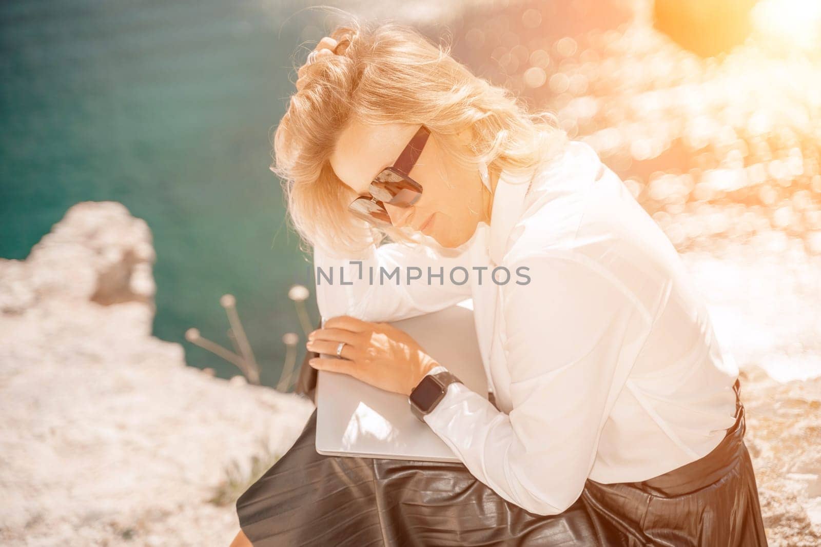 Business woman on nature in white shirt and black skirt. She works with an iPad in the open air with a beautiful view of the sea. The concept of remote work