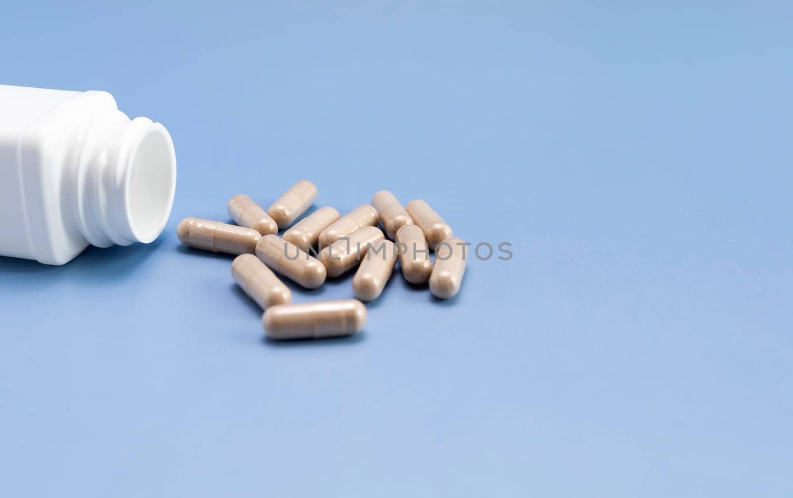 Scattered Pills, Capsules OF Slippery Elm, White Bottle, Container On Blue Background. Dietary Nutritional Supplement, Medication. Ulmus Fulva, Herbal Remedy Concept. Horizontal, Copy space For Text.