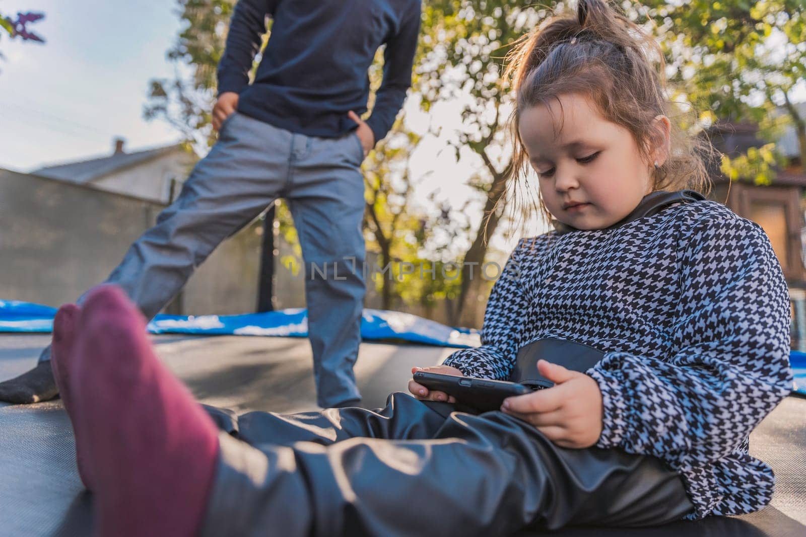 portrait of children who sit on a trampoline and look at the phone