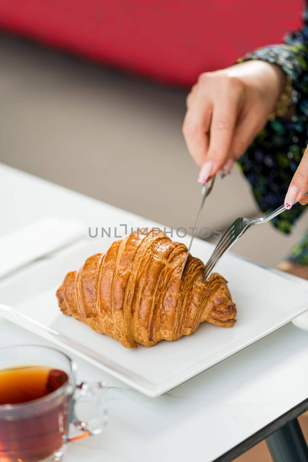 Croissant on a white porcelain plate with tea on the side by Sonat