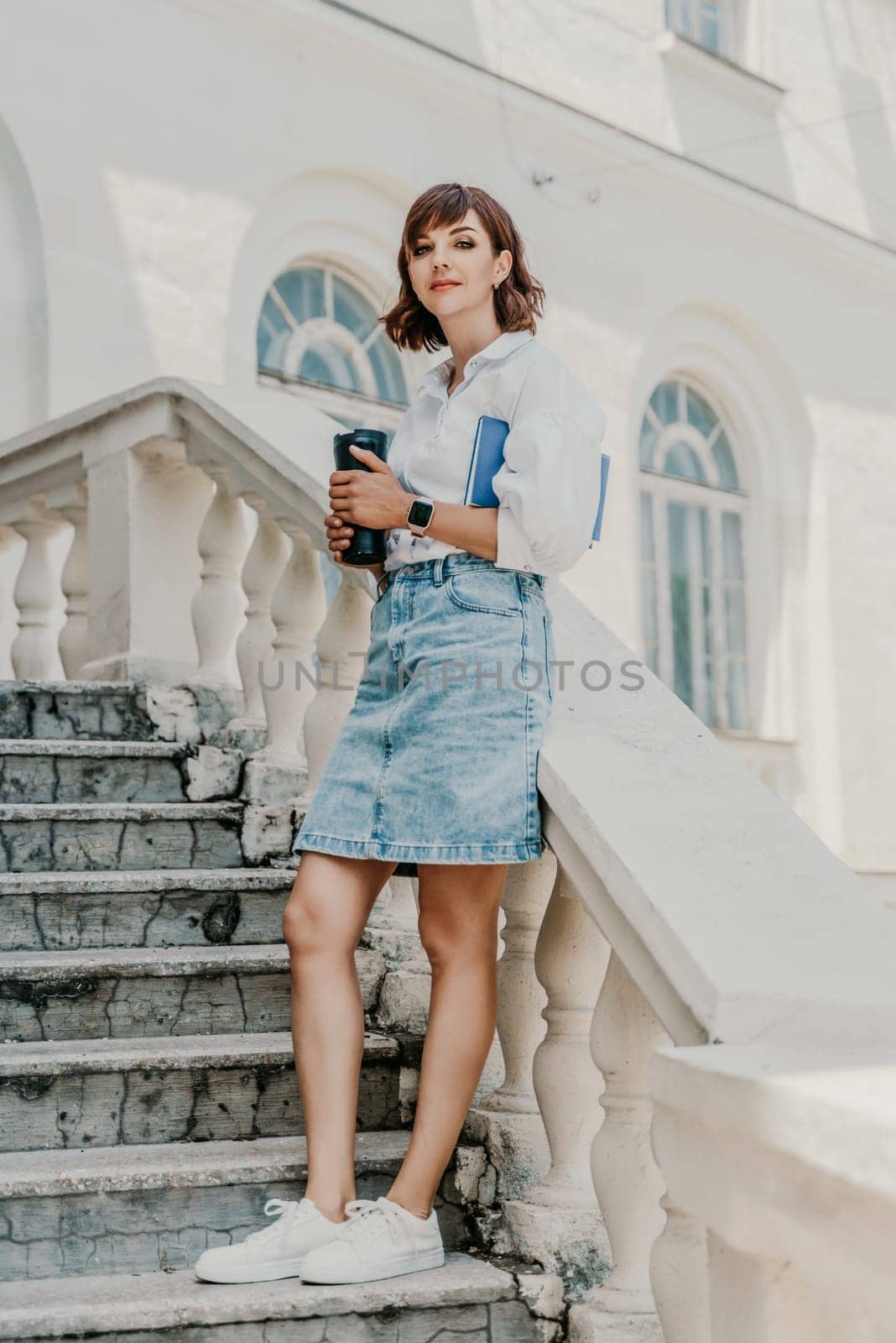 Woman building city. A business woman in a white shirt and denim skirt stands leaning against the wall on the steps of an ancient building in the city.