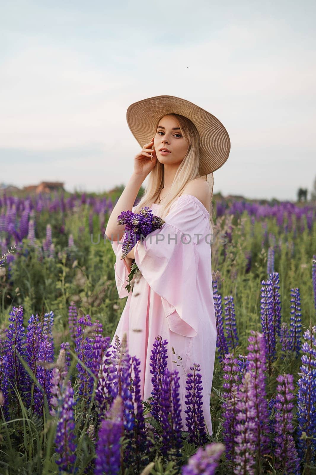 A beautiful woman in a straw hat walks in a field with purple flowers. A walk in nature in the lupin field by Annu1tochka