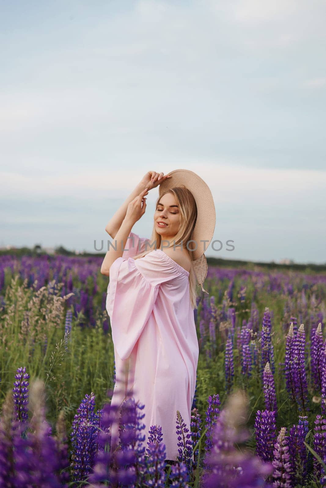 A beautiful woman in a straw hat walks in a field with purple flowers. A walk in nature in the lupin field by Annu1tochka