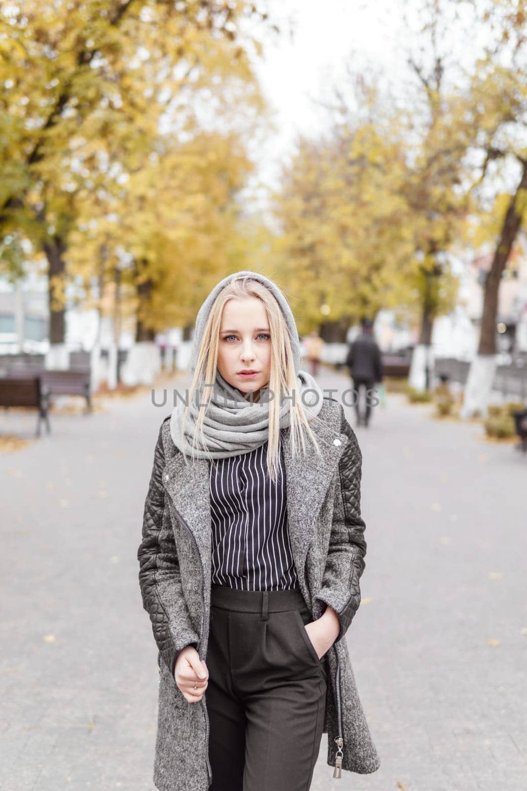 A young blonde walks through the autumn city in a gray coat. The concept of urban style and lifestyle