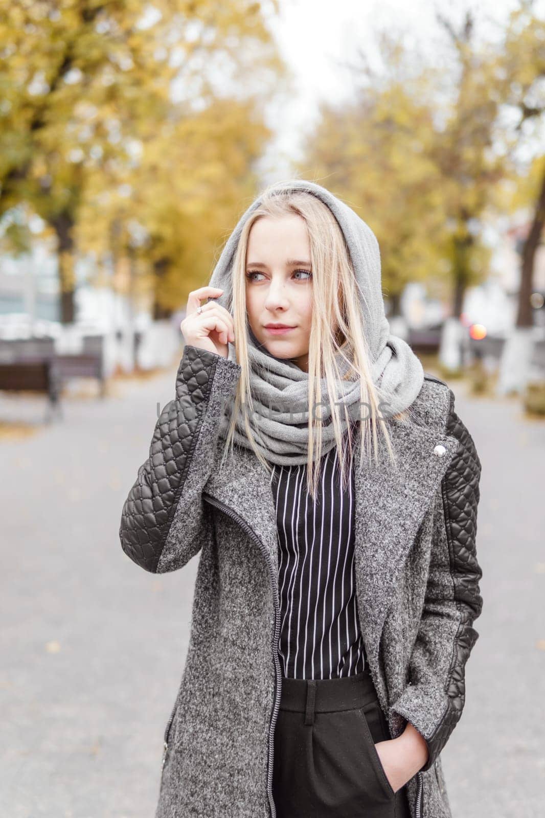 A young blonde walks through the autumn city in a gray coat. The concept of urban style and lifestyle