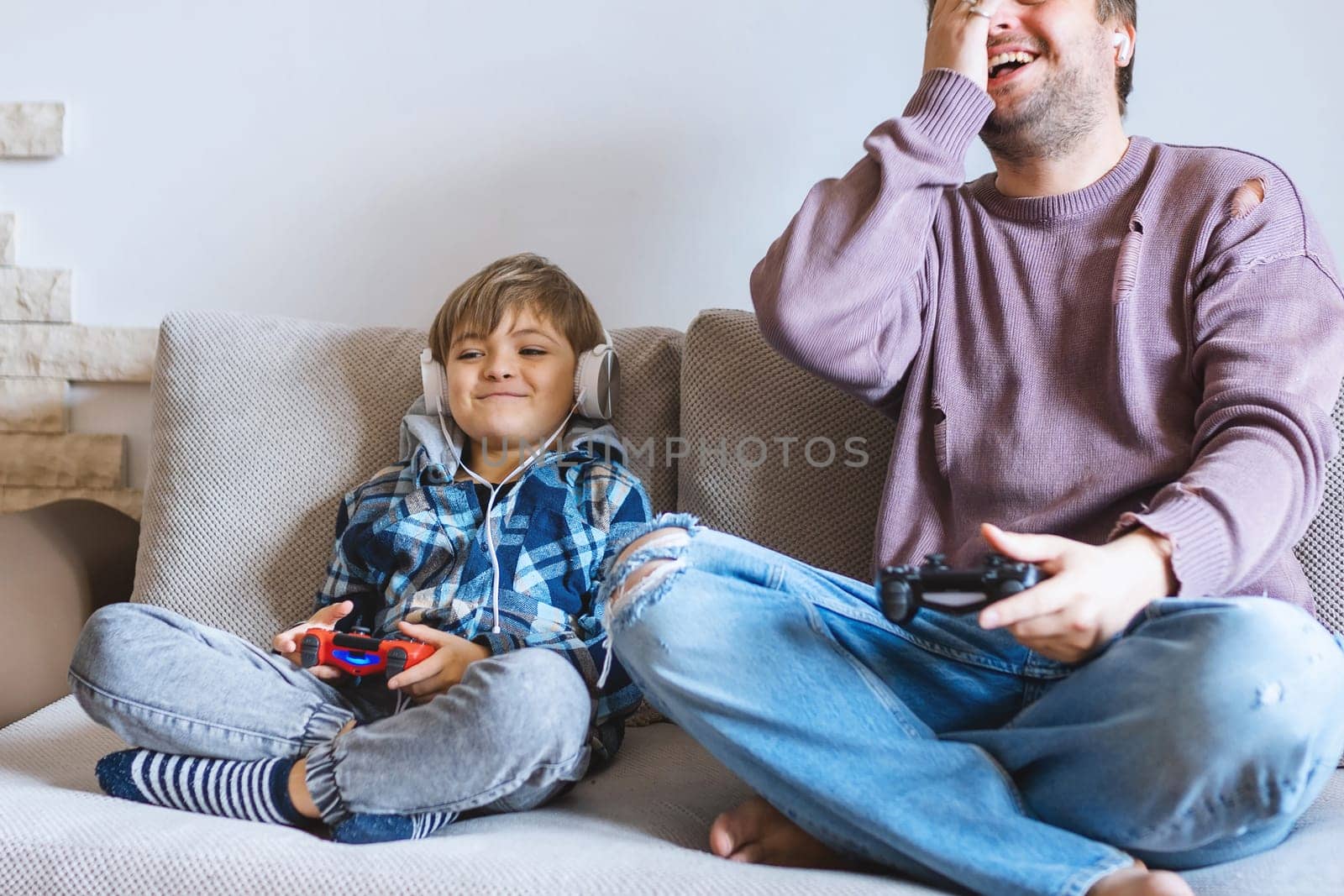 Father And Son Sitting On Sofa In Lounge Playing Video Game.