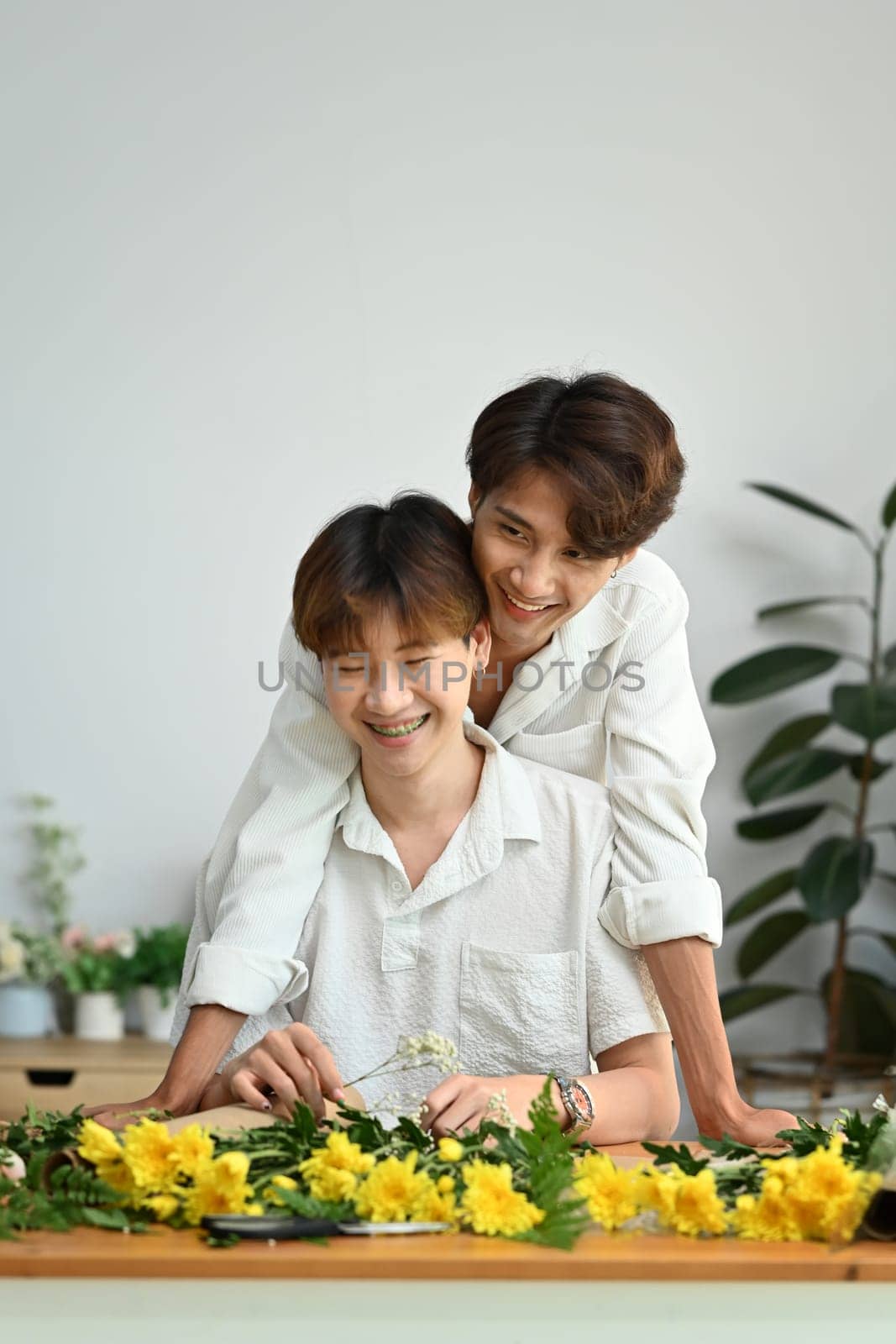 LGBT, love moments and lifestyle concept. Affectionate male gay couple spending time together, enjoying arranging flowers in cozy home by prathanchorruangsak