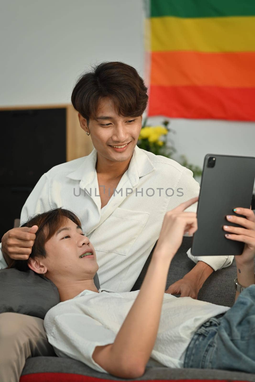 Loving homosexual couple embracing and using digital tablet on couch. LGBT, love and lifestyle relationship concept by prathanchorruangsak