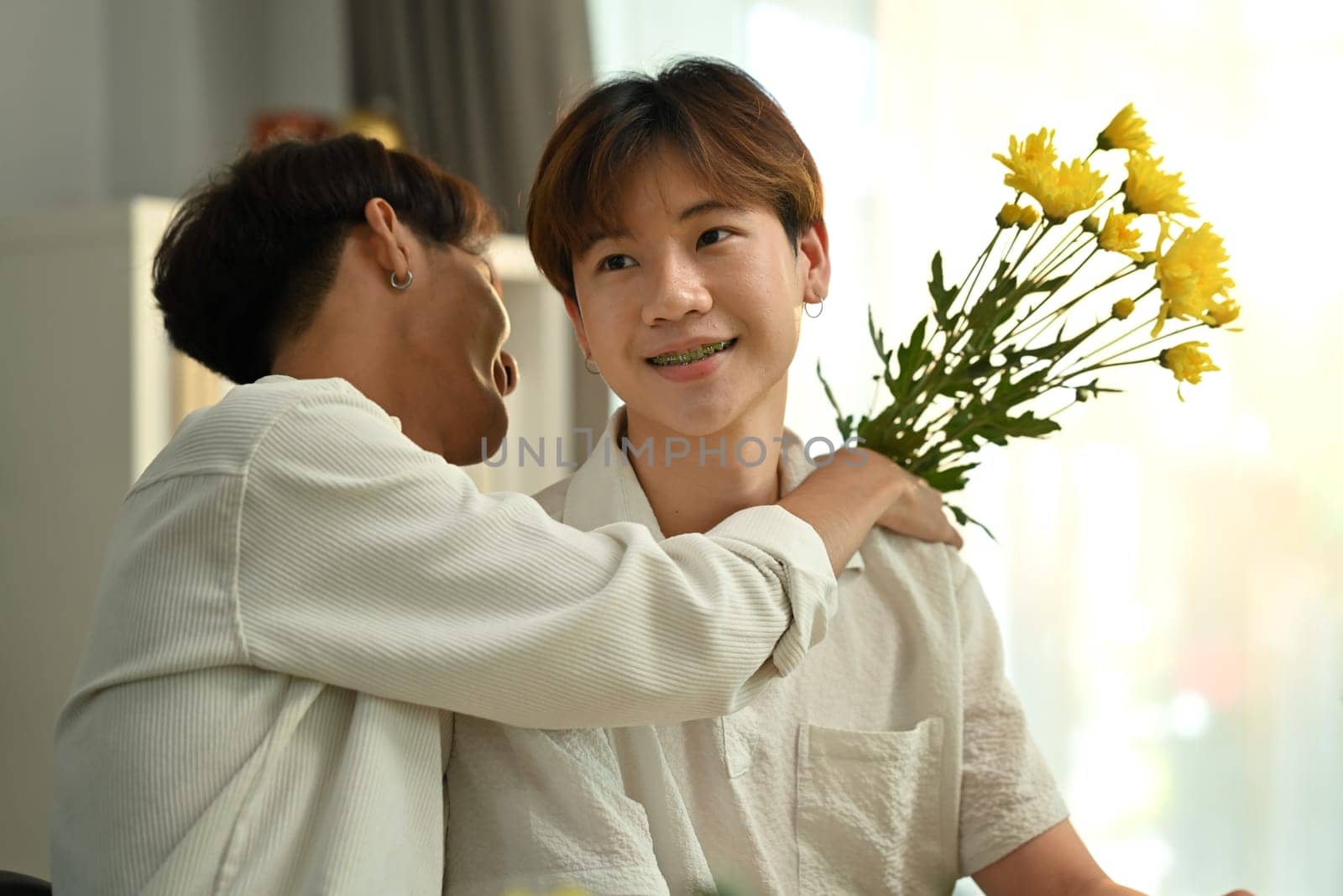 Shot of romantic asian man giving a bunch of flowers to his boyfriend. LGBTQ people lifestyle and love emotion by prathanchorruangsak