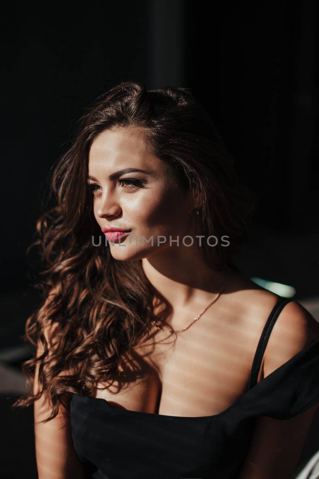 Portrait of a sexy brunette in a black dress on a dark background. girl takes off her dress slowly in the bedroom.