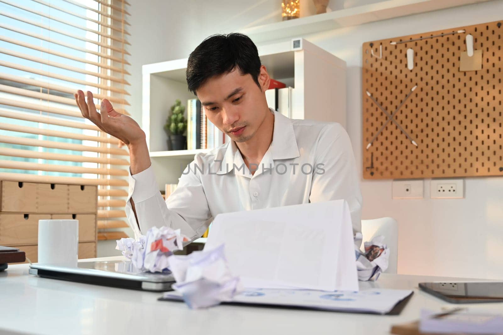 Exhausted male employee working with annual financial report at his workplace. Failure business, overwork concept by prathanchorruangsak