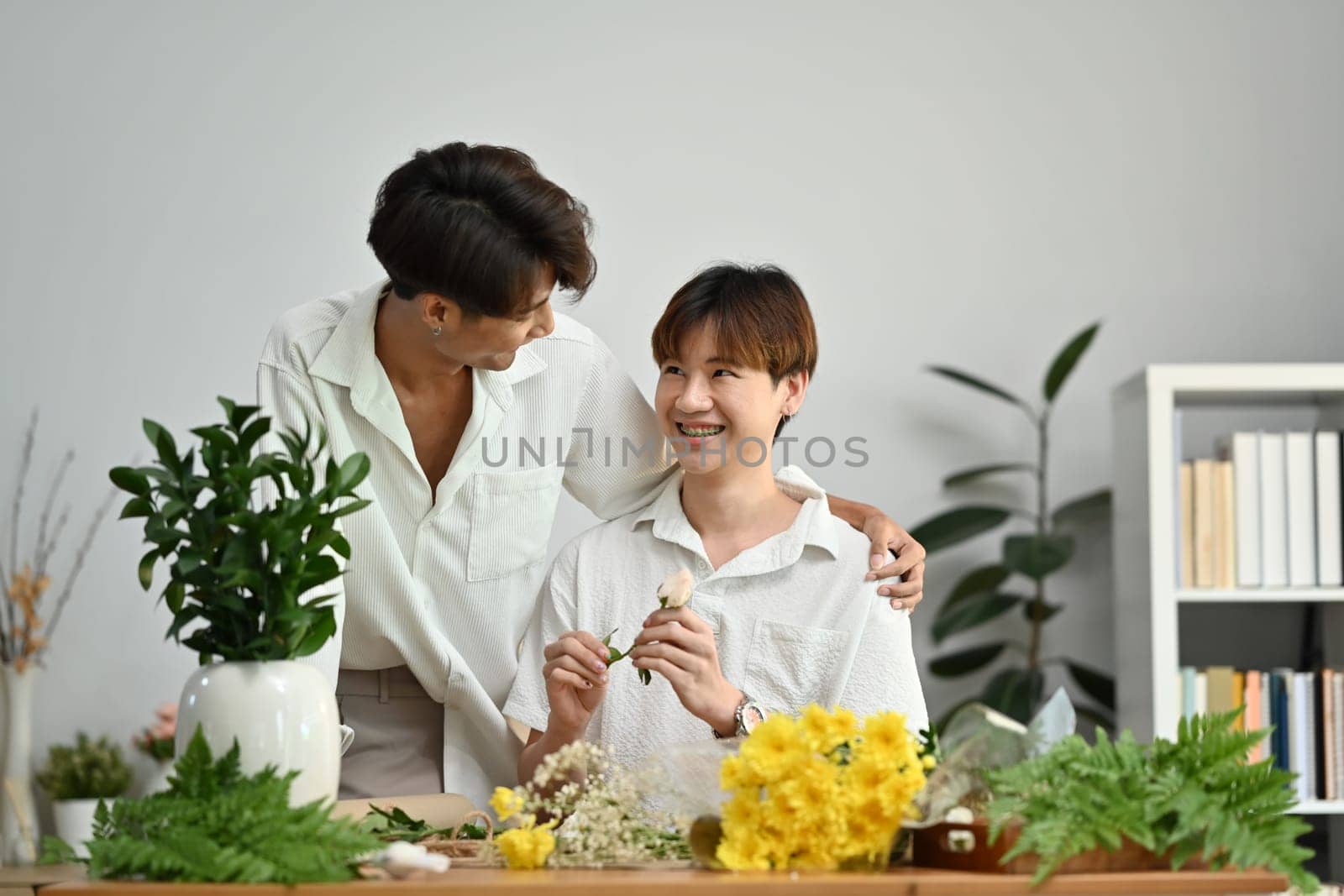 LGBT, love moments and lifestyle concept. Affectionate male gay couple spending time together, enjoying arranging flowers in cozy home by prathanchorruangsak