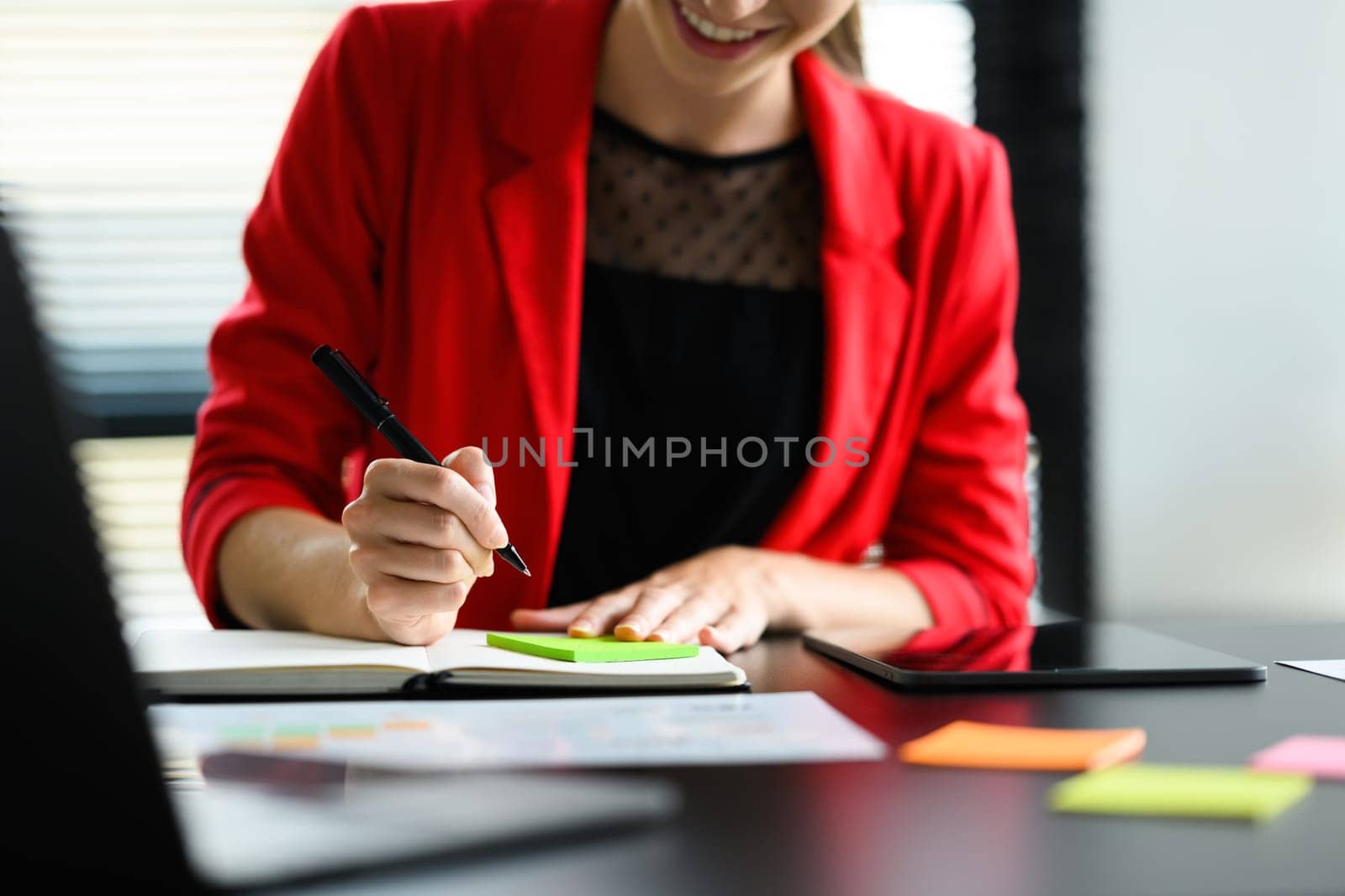 Professional businesswoman in red suit writing hers strategy ideas on sticky notes at office desk by prathanchorruangsak