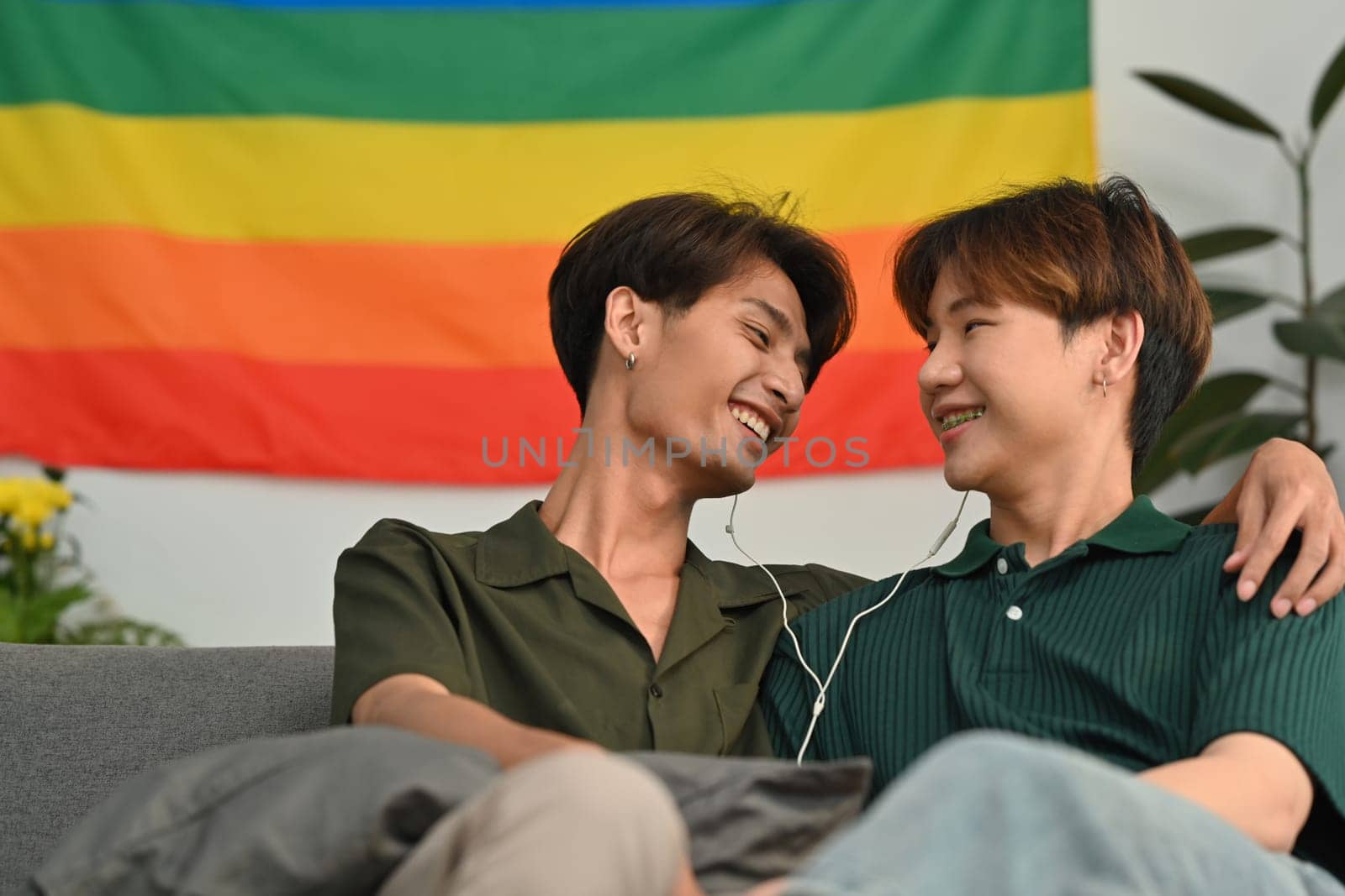 Carefree male gay couple listening to music on earphones, spending time together at home. LGBT, relationship and comfort living concept.