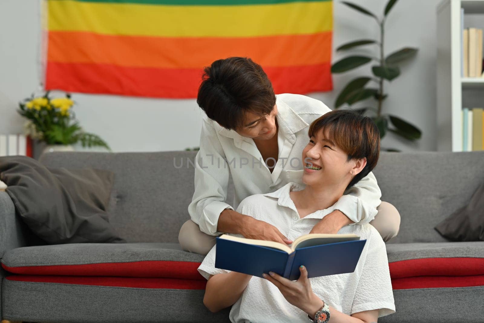 Happy moment of two young male lovers embracing each other and reading book in living room. Homosexual and love concept.