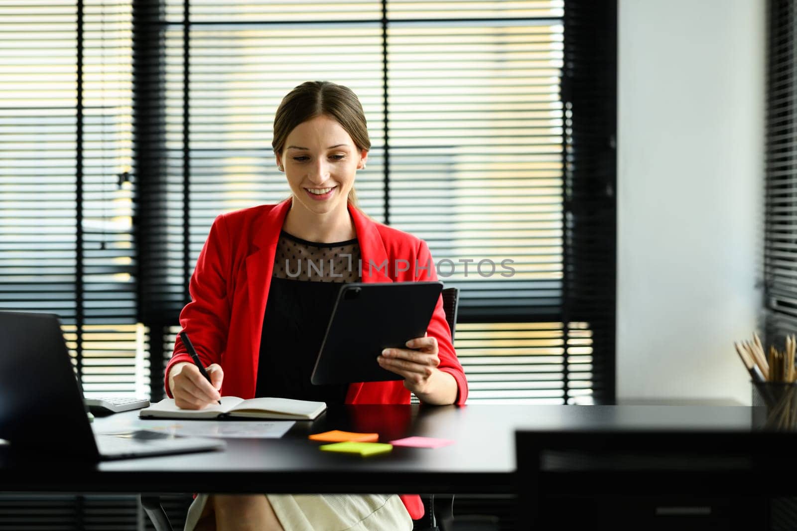 Gorgeous female entrepreneur in luxury suit using digital tablet, working online sale marketing at modern workplace by prathanchorruangsak