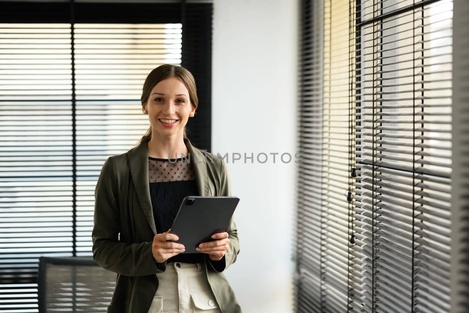 Beautiful caucasian female executive wearing formal stylish clothes holding digital tablet standing at her workplace.