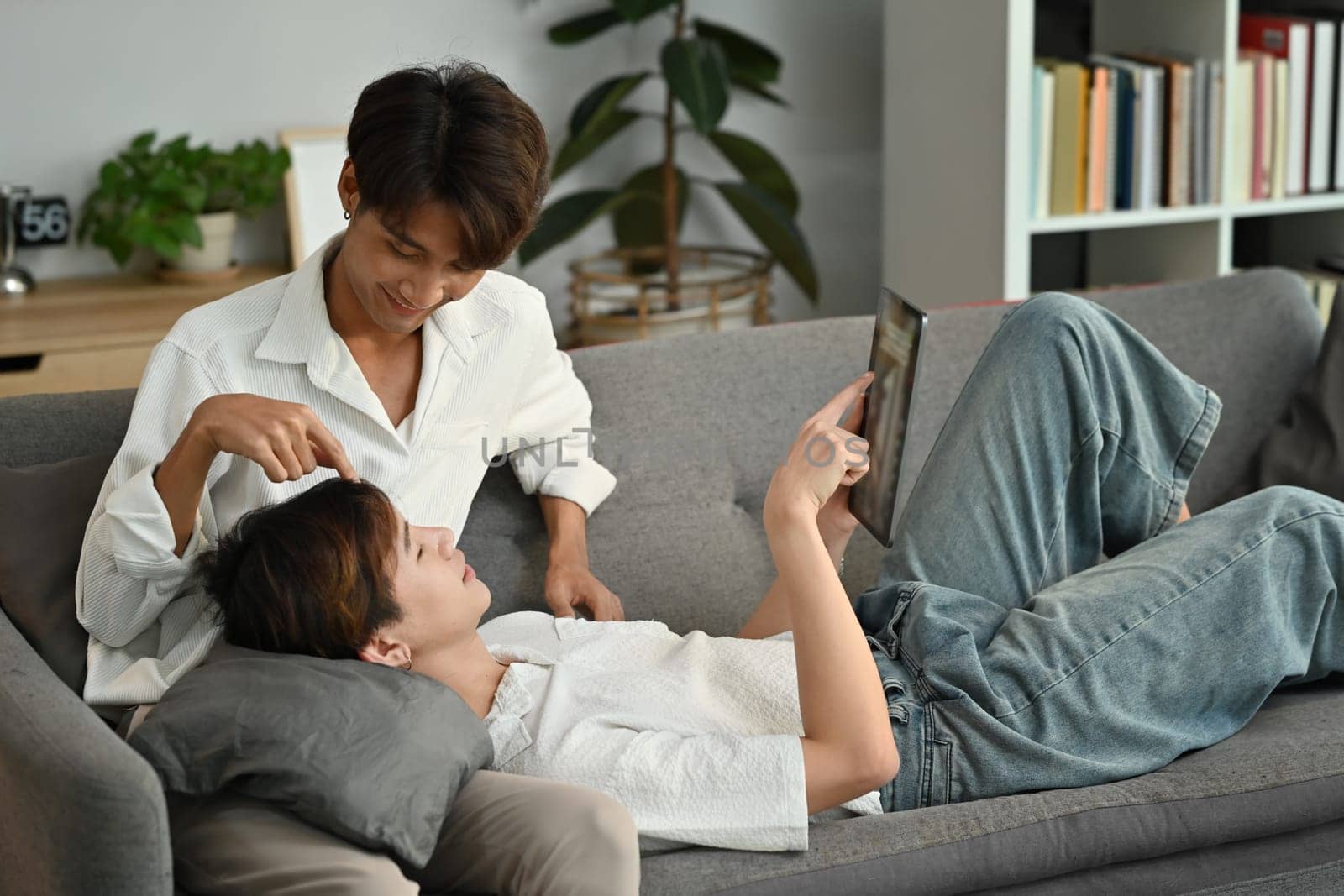 Loving homosexual couple embracing and using digital tablet on couch. LGBT, love and lifestyle relationship concept by prathanchorruangsak