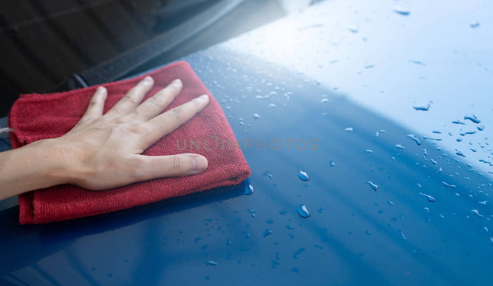 Car wash service. Man hand holding red microfiber cloth polish blue car and water drop after cleaning. Auto care service business concept. Man cleaning and detailing luxury car with microfiber cloth. by Fahroni