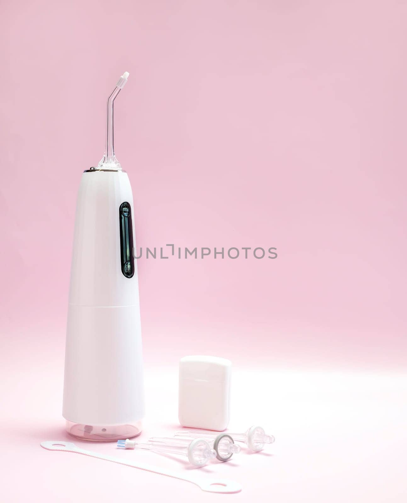 Oral hygiene set. Oral teeth irrigator, nozzles, dental floss, tongue scraper. Pink background. Dental care, treatments, daily routine. Vertical plane, closeup, space for text by netatsi