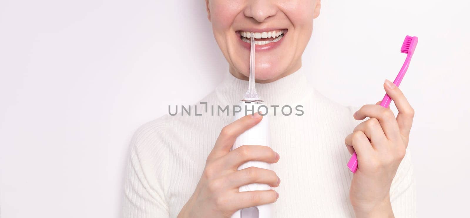 Cropped smiling with ideal teeth woman holds oral irrigator, toothbrush on white background.Caucasian girl keeps white healthy teeth with oral cleaning, flossing,brushing Dentistry,dental care concept by netatsi