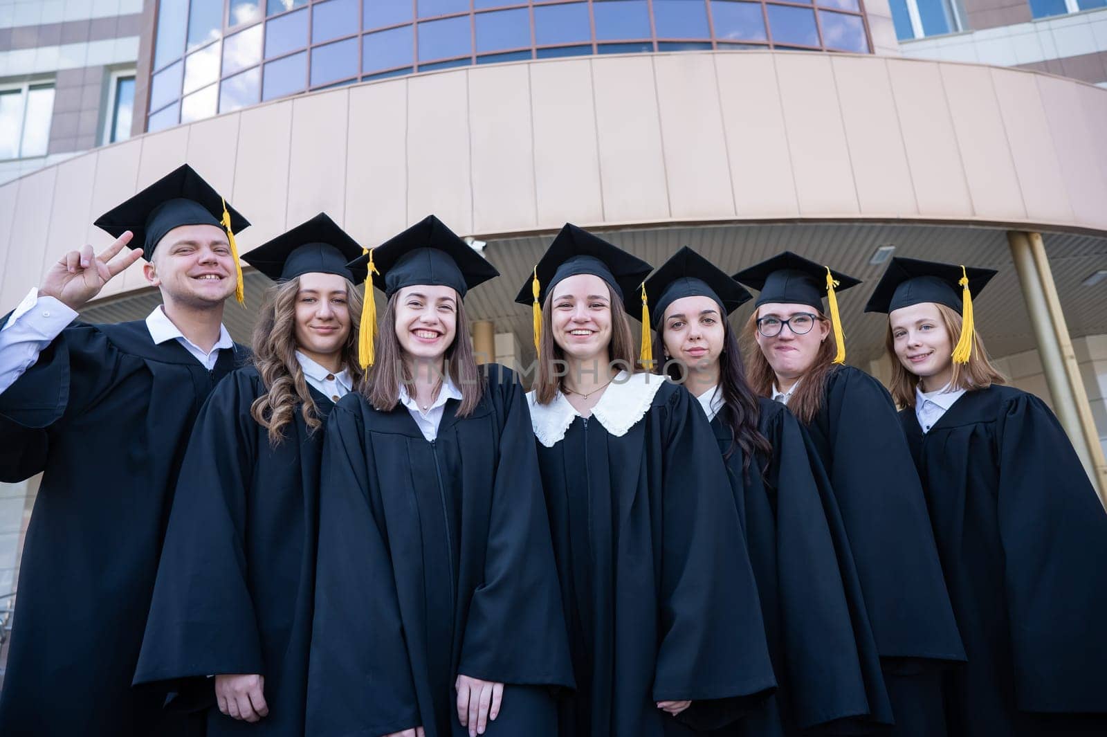 Happy students in graduate gown stand in a row against the backdrop of the university