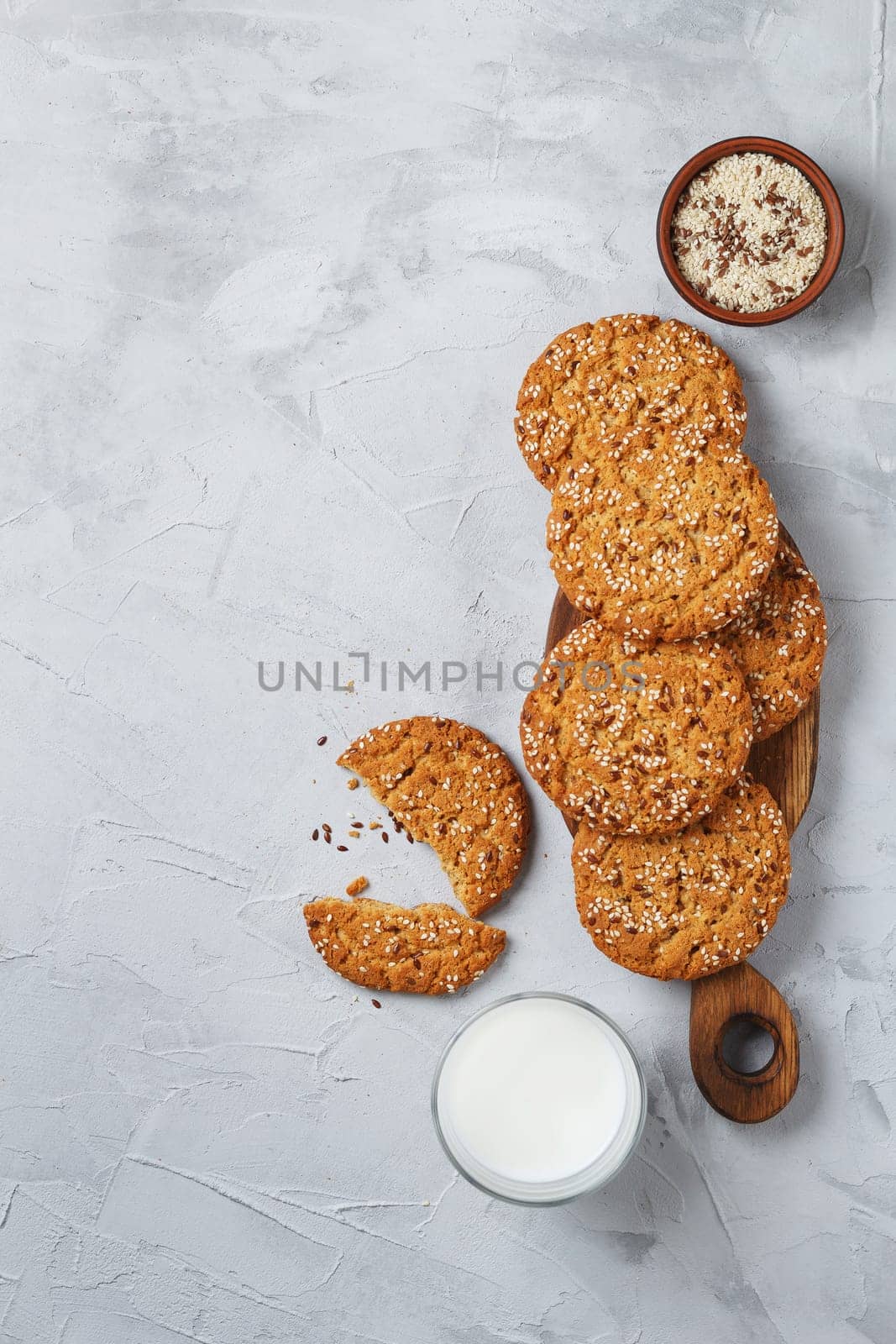 Oatmeal cookies with sesame seeds and flax seeds on a gray background with a jar of oatmeal and a glass of milk.Copy space by lara29