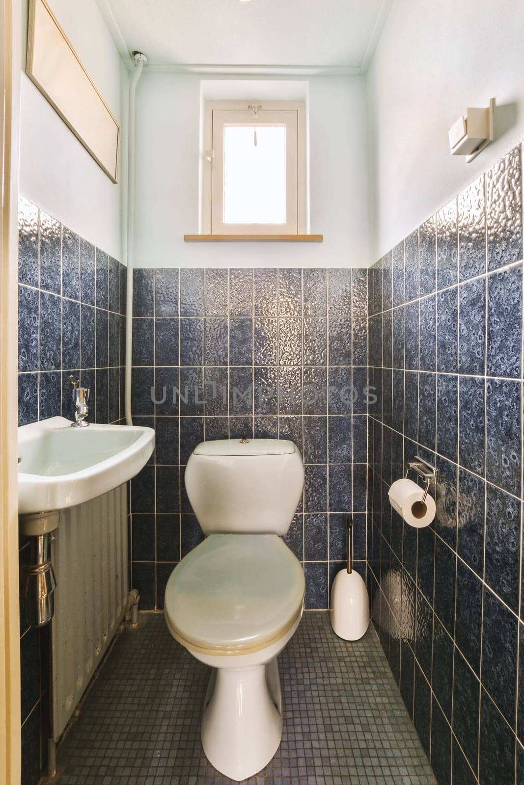 a small bathroom with blue tiles on the walls and white fixtures in the toilet bowl is next to the sink