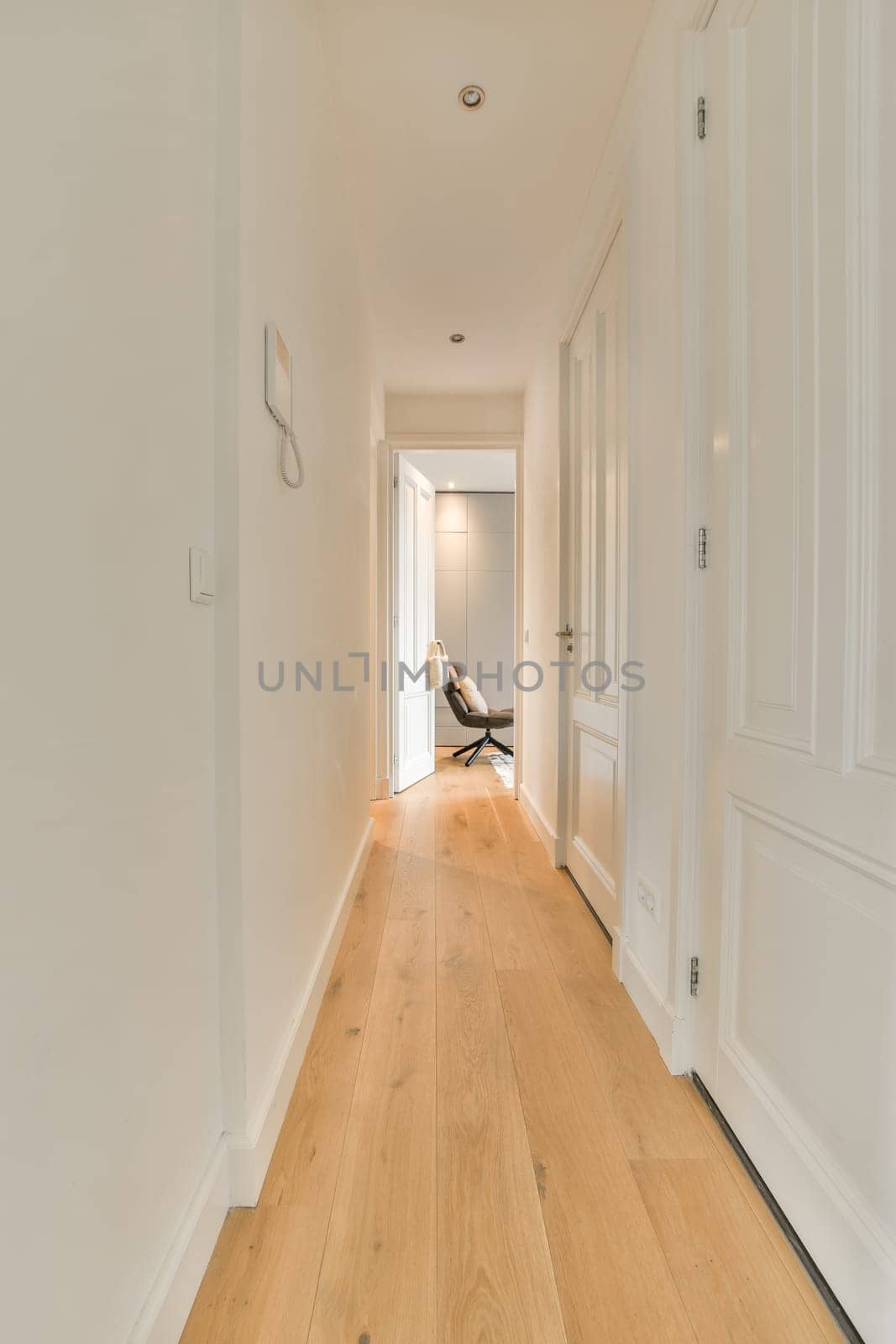 a long hallway with white walls and wood flooring on either side by side, leading to the front door