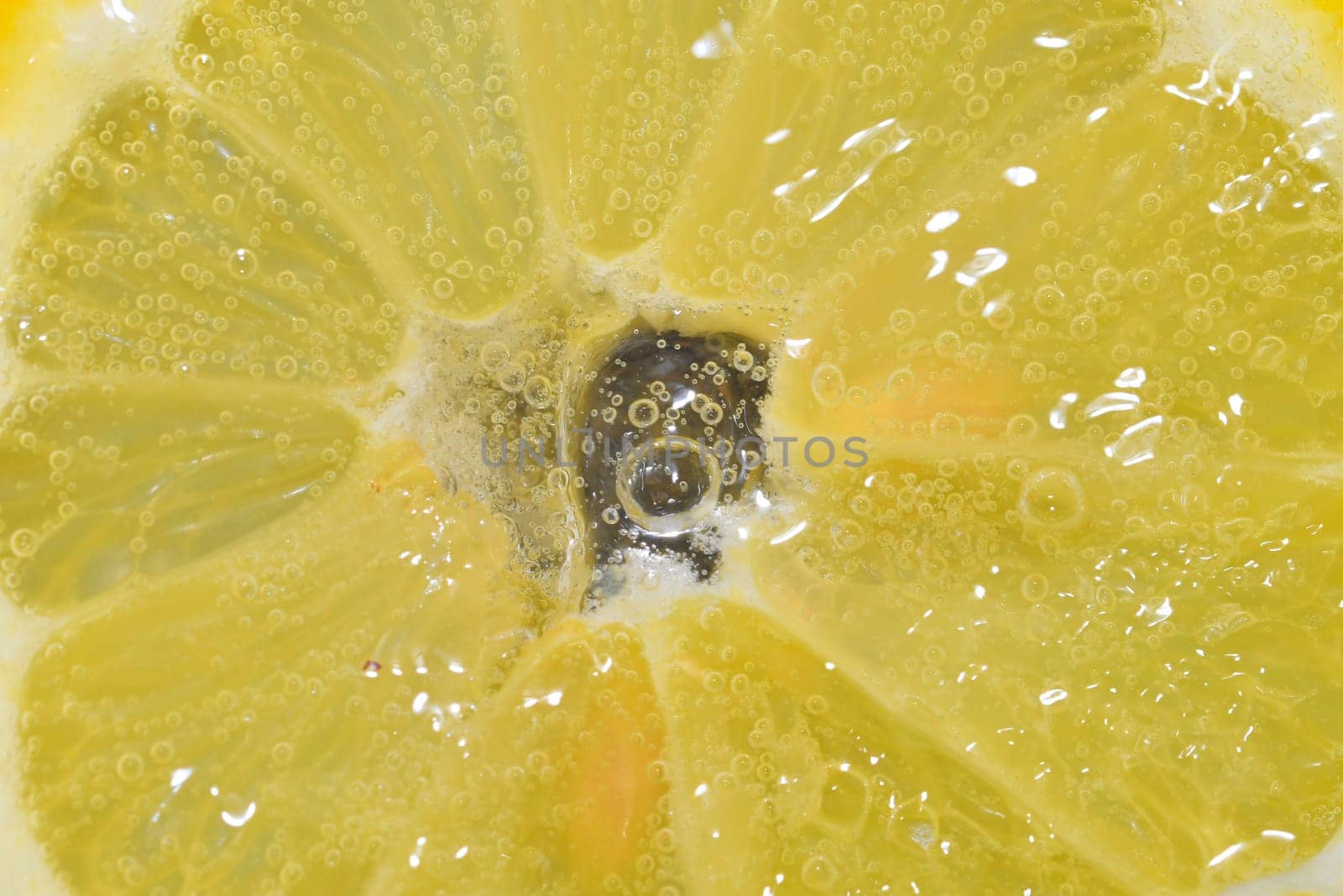 Slice of ripe lemon in water. Close-up of lemon in liquid with bubbles. Slice of ripe citron in sparkling water. Macro image of fruit in carbonated water