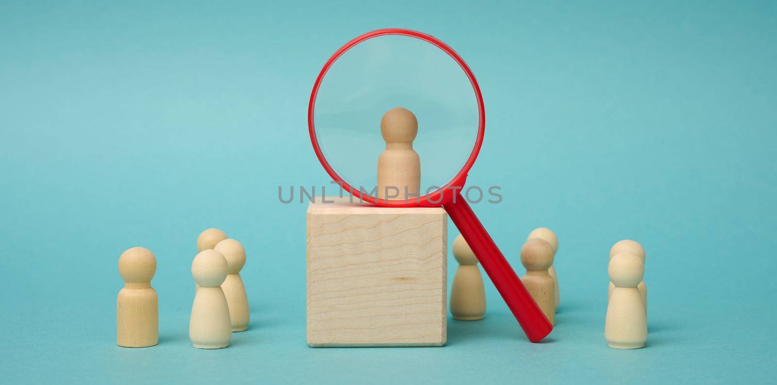 wooden figures of men stand on a beige background and a plastic magnifying glass. Recruitment concept, search for talented and capable employees by ndanko