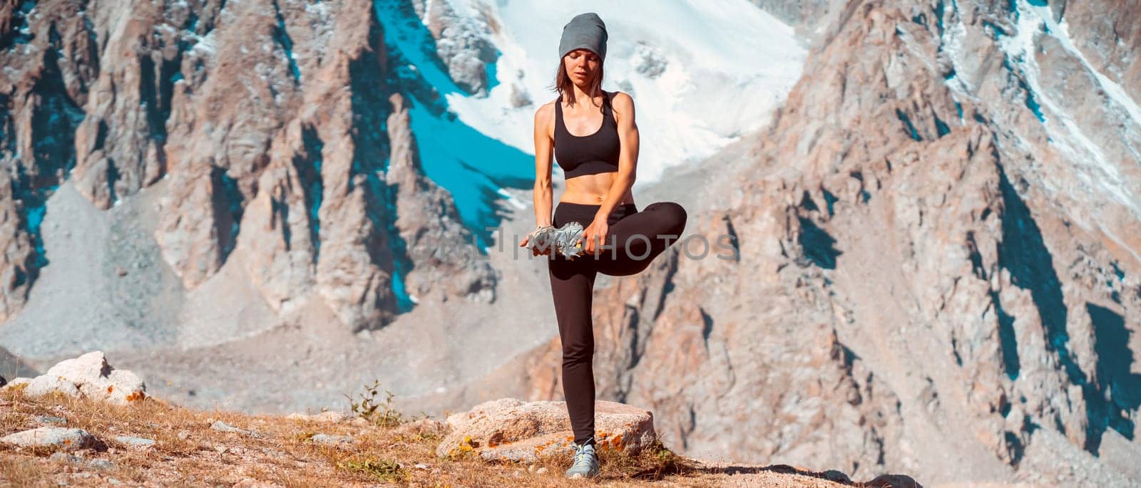 A young sports girl practices yoga on a background of snow-capped mountains on a sunny day, a woman does exercises, trains and meditates in a picturesque mountainous area.