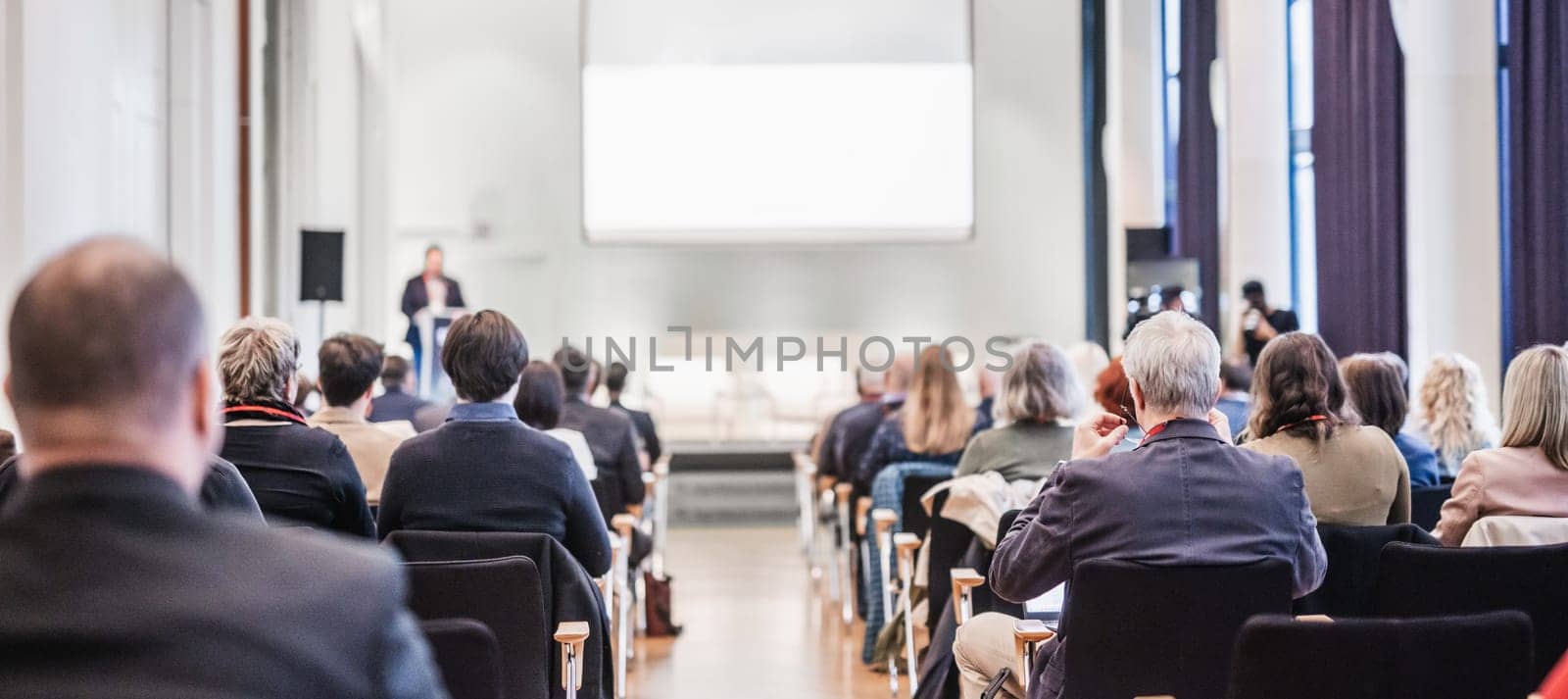 Speaker giving a talk in conference hall at business event. Rear view of unrecognizable people in audience at the conference hall. Business and entrepreneurship concept