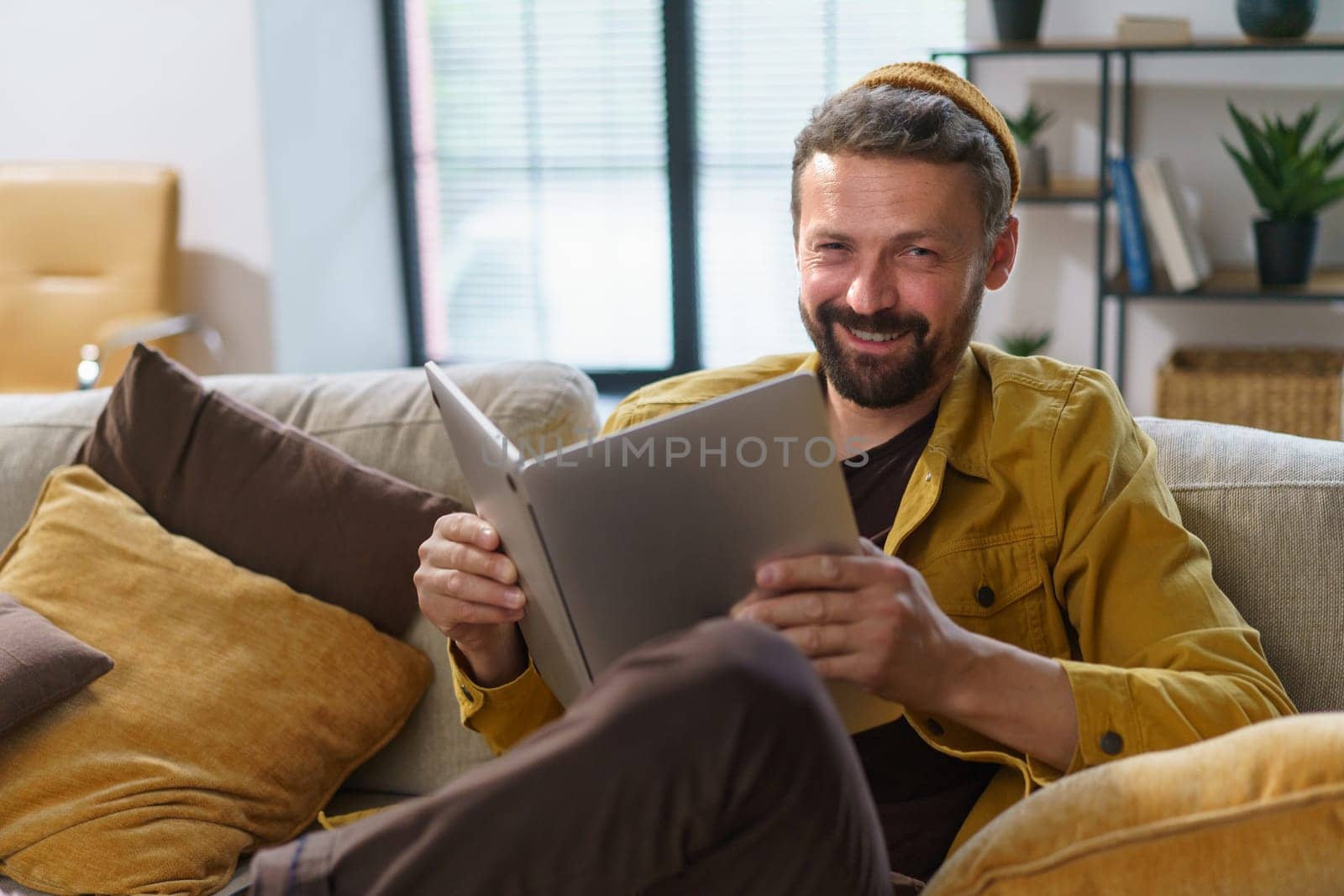 Student engaging in deceptive behavior sit on sofa and hold laptop like book indoors. Concept of cheating, highlighting student's questionable actions in academic context. High quality photo