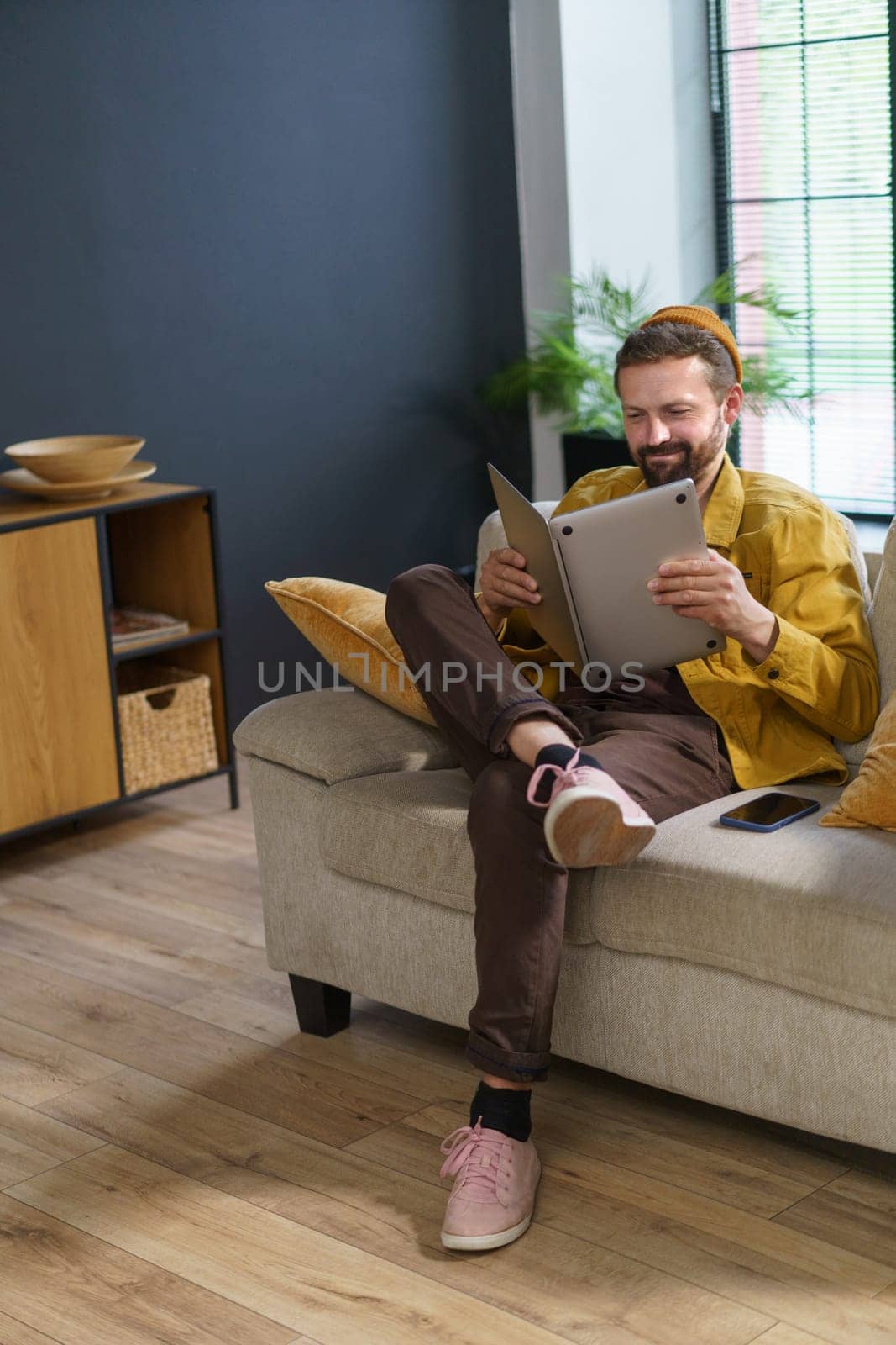 man sitting with laptop in incorrect position, showcasing ineptitude as worker. Man's lack of proper work habits and efficiency reads laptop like book, displaying misguided approach to using device. by LipikStockMedia