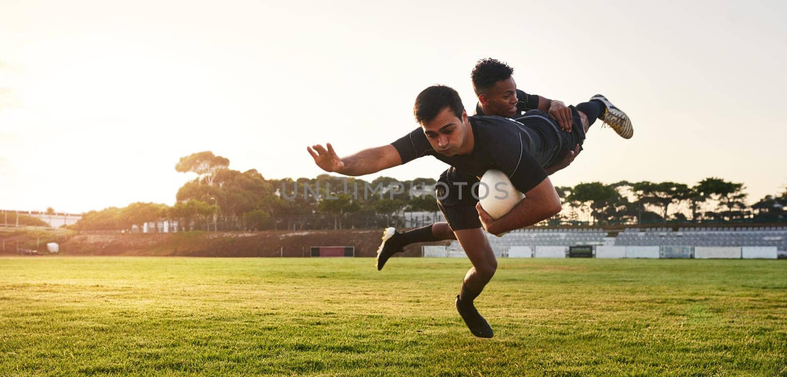 Hes got me. Full length shot of two handsome sportsmen playing rugby during a training session during the day. by YuriArcurs