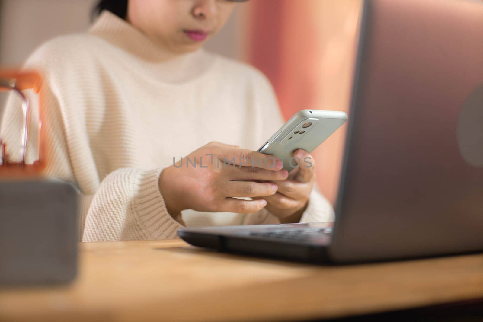 Young Asian woman using smartphone and working sitting in office at home close-up.