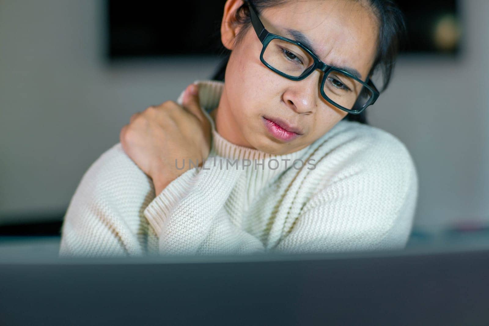 Young Asian woman feeling pain in her neck and shoulders after working for a long time on her laptop. Office syndrome concept.