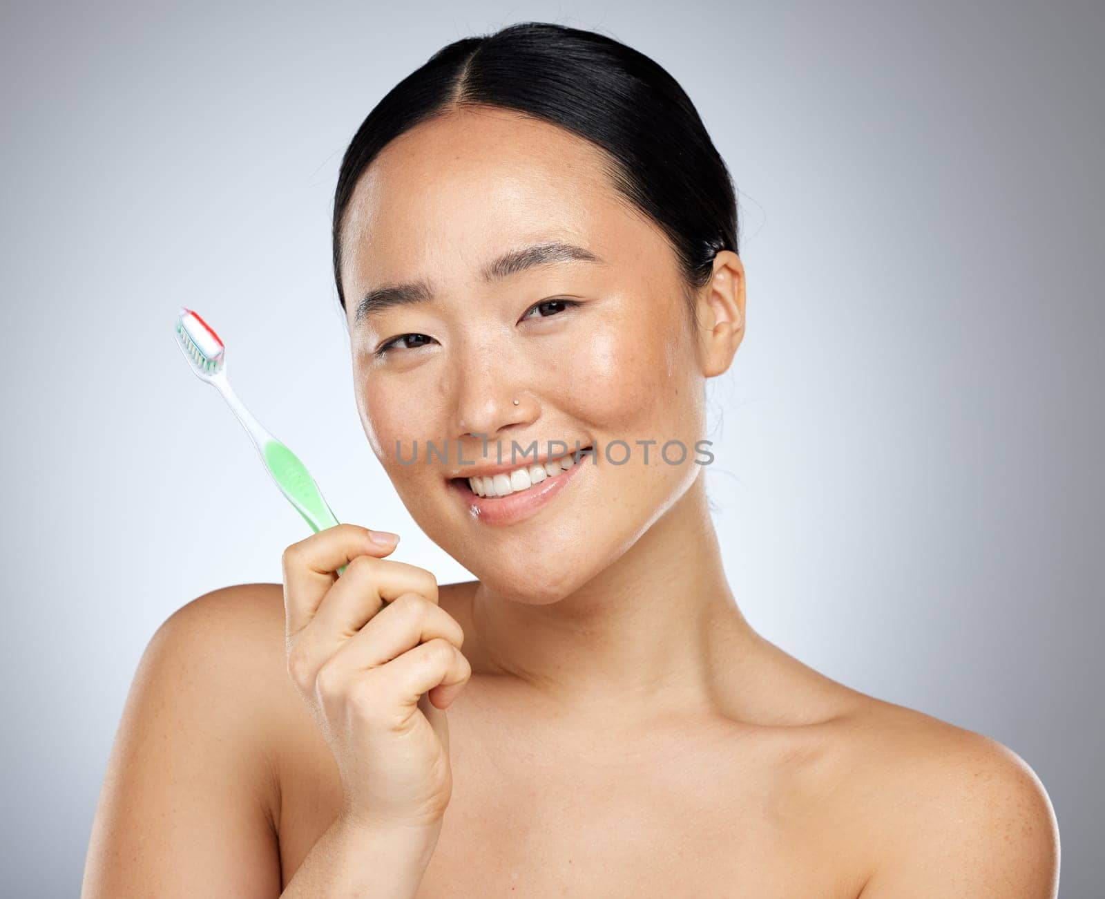 Beauty, dental care and oral hygiene with an asian woman in studio on a gray background with a smile. Portratit, teeth and toothbrush with a young female brushing her teeth for health or wellness.