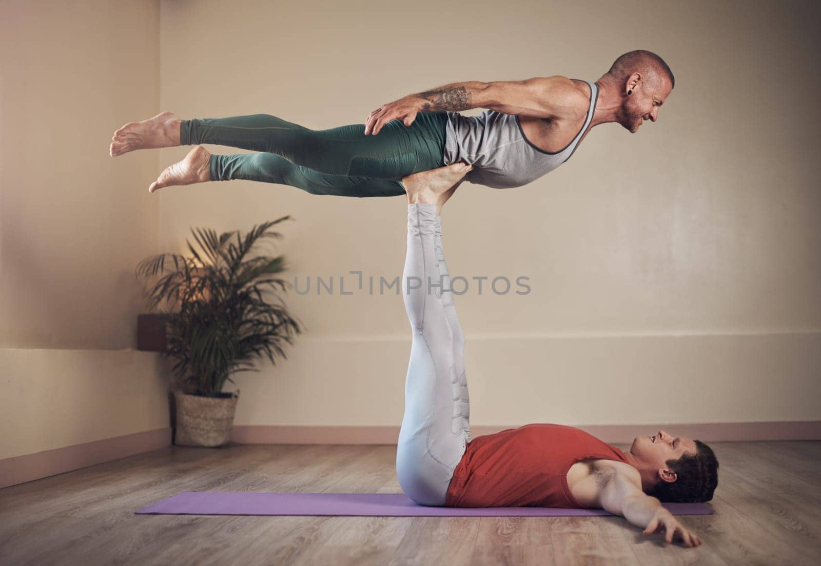 Working those legs. Full length shot of a handsome young man doing acro yoga with his partner in a yoga studio. by YuriArcurs