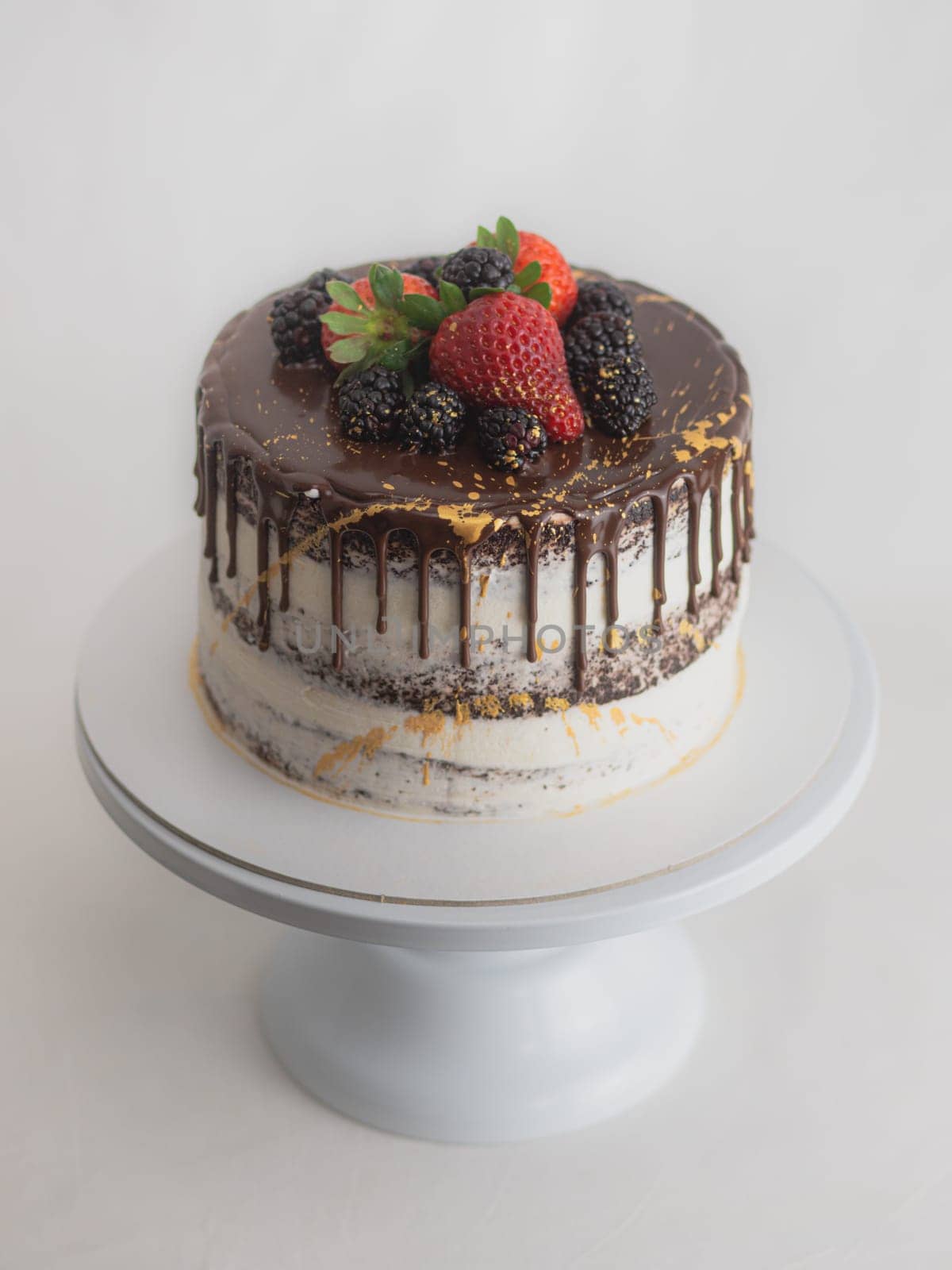 studio shot of chocolate frosted dripped icing cup cake with sweet fruit topping and golden brush strokes