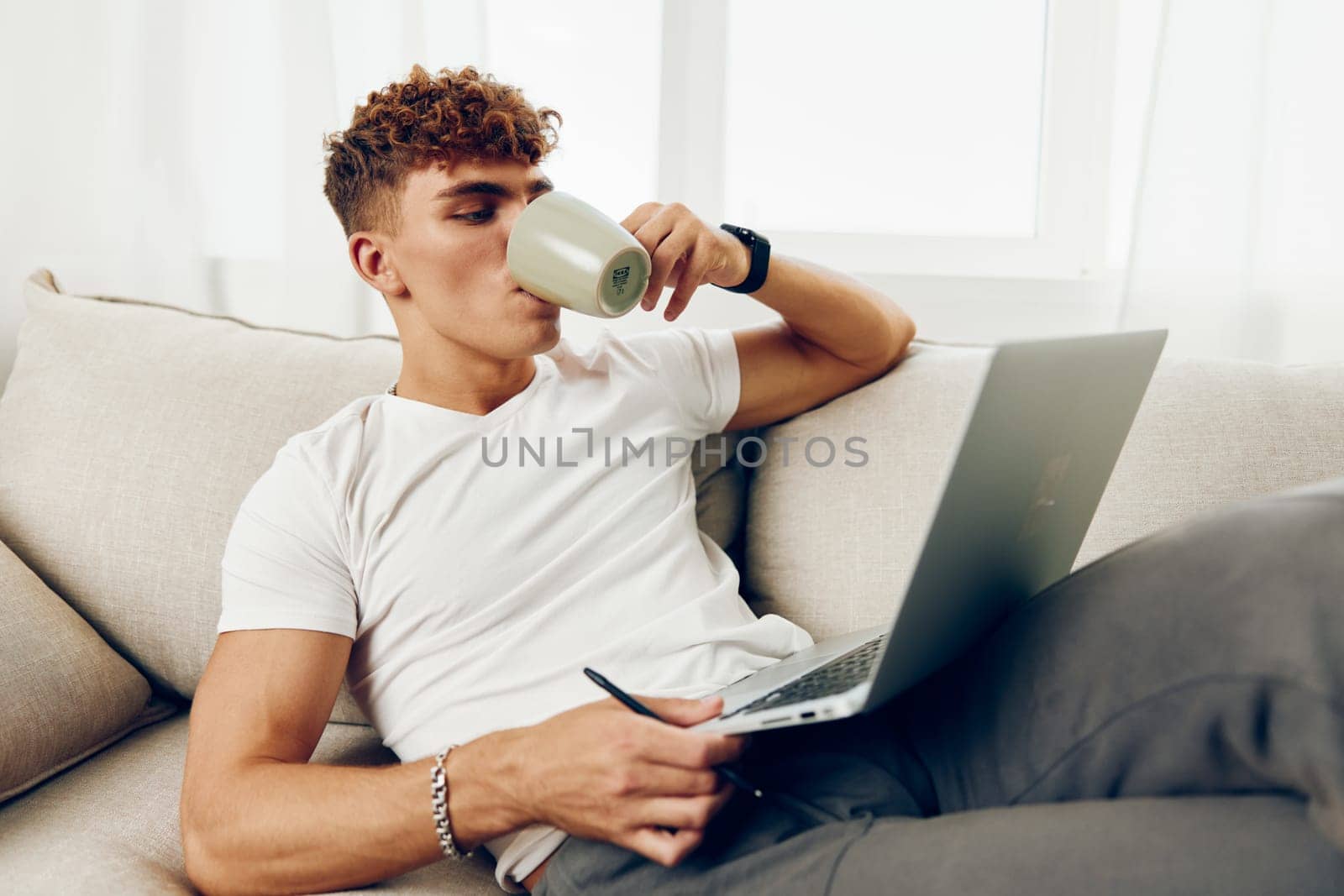 man interior technology sitting home call person lifestyle modern caucasian laptop phone t-shirt room browsing looking typing male notebook