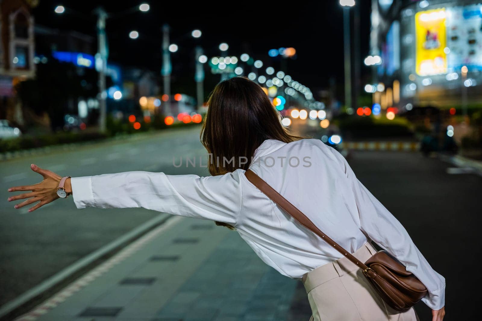 Asian business woman hail waving hand taxi on road in city street at night, Beautiful woman smiling using smartphone application hailing with hand up calling cab outdoor after late work, back view