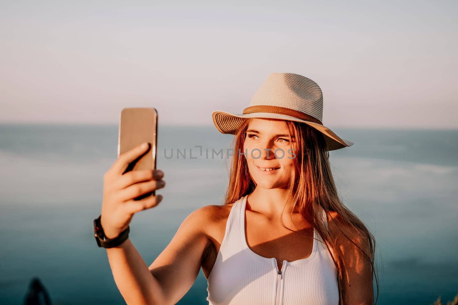 Woman travel sea. Happy tourist in hat enjoy taking picture outdoors for memories. Woman traveler posing on the beach at sea surrounded by volcanic mountains, sharing travel adventure journey