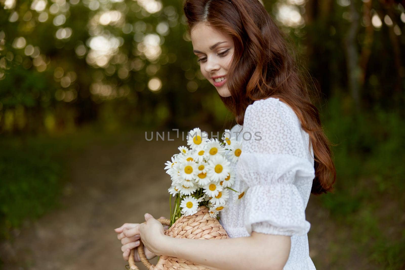 close portrait of a happy, red-haired woman with a wicker basket full of daisies in nature. High quality photo