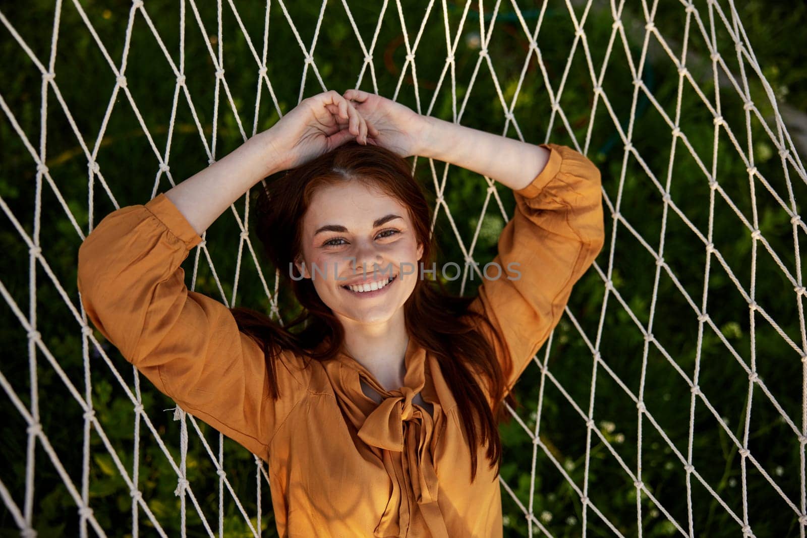 a close horizontal photo from above of a happy, pleasantly smiling woman lying on a mesh hammock in nature on a sunny day. High quality photo