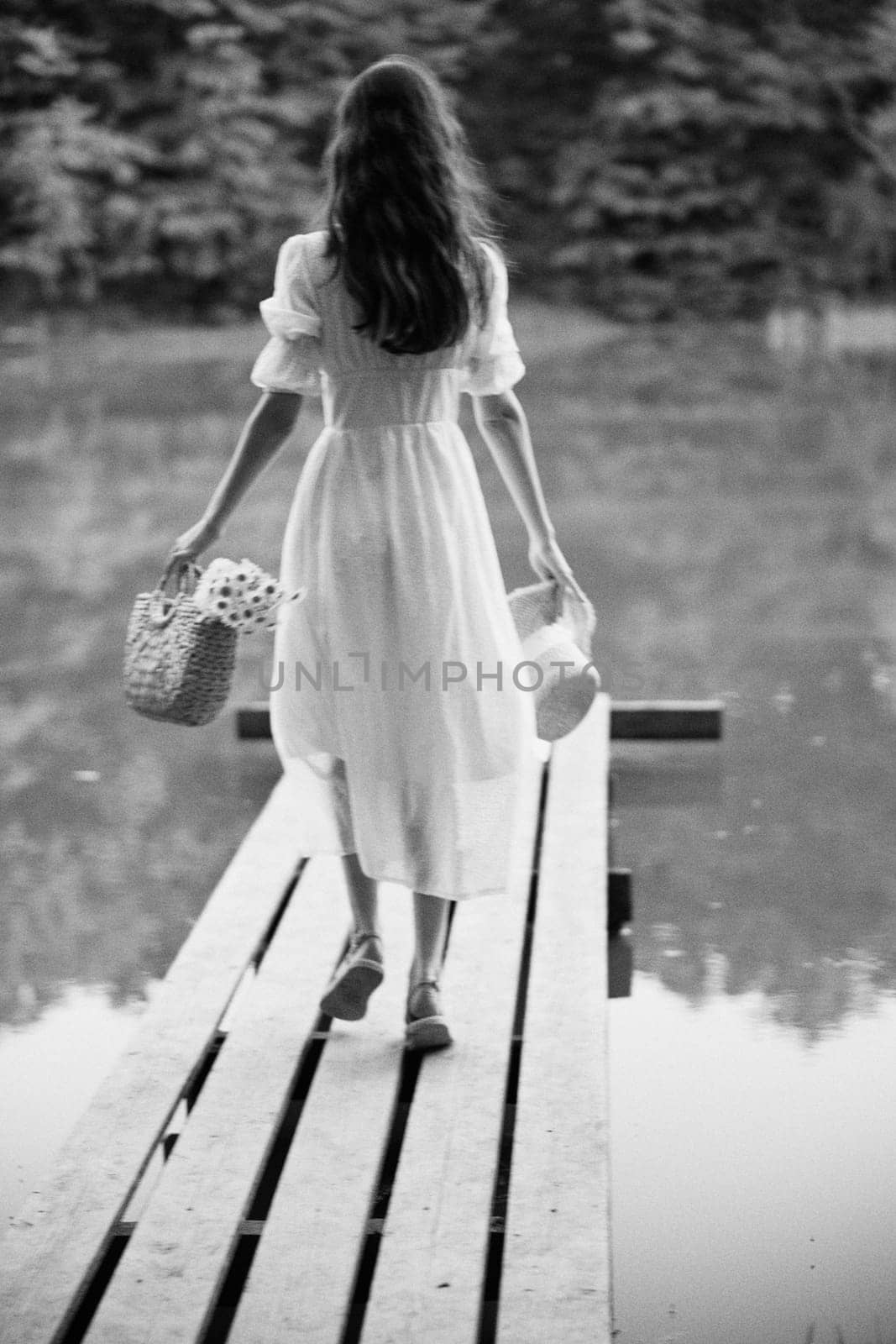 a woman in a long light dress walks along the pier of a forest lake. monochrome photography. High quality photo