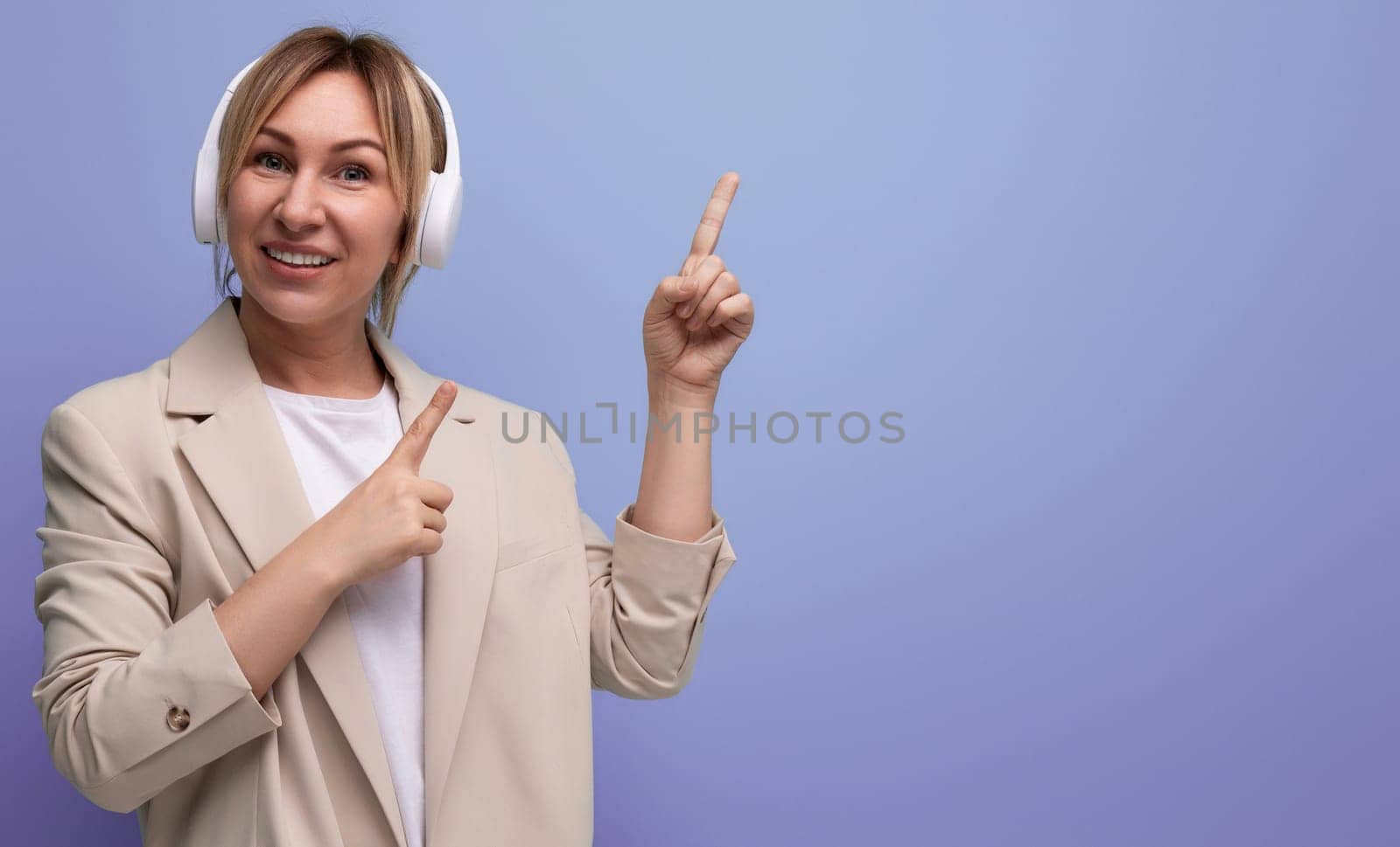 portrait of young woman in wireless headphones pointing finger at copy space studio background.